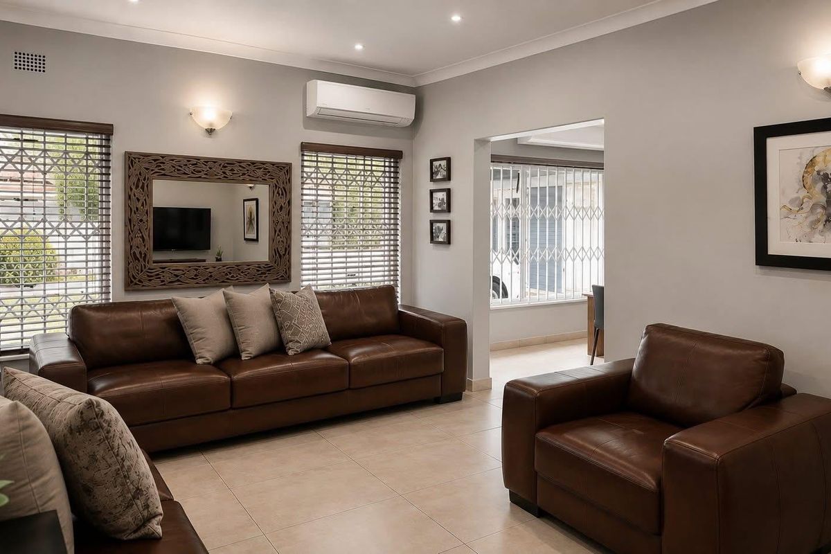 A well-maintained living room featuring tiled flooring, recessed downlighting, and a wall-mounted air conditioning unit, with natural light provided by windows with venetian blinds.