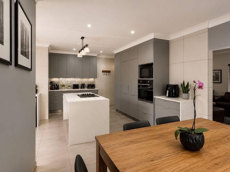 Modern open-plan kitchen featuring a central island, sleek grey cabinetry, built-in appliances, and tiled flooring, seamlessly flowing into the adjacent living area.