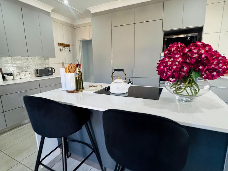 Modern kitchen featuring a central island with quartz countertops, induction cooktop, sleek grey cabinetry, and contemporary pendant lighting.