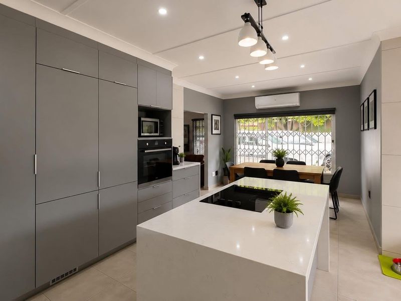 Modern open-plan kitchen featuring a central island with induction cooktop, sleek grey cabinetry, built-in appliances, and tiled flooring throughout.
