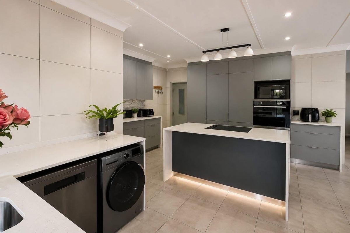 Modern, high-end kitchen featuring sleek grey cabinetry, a central island with integrated cooktop, stone countertops, and premium built-in appliances.