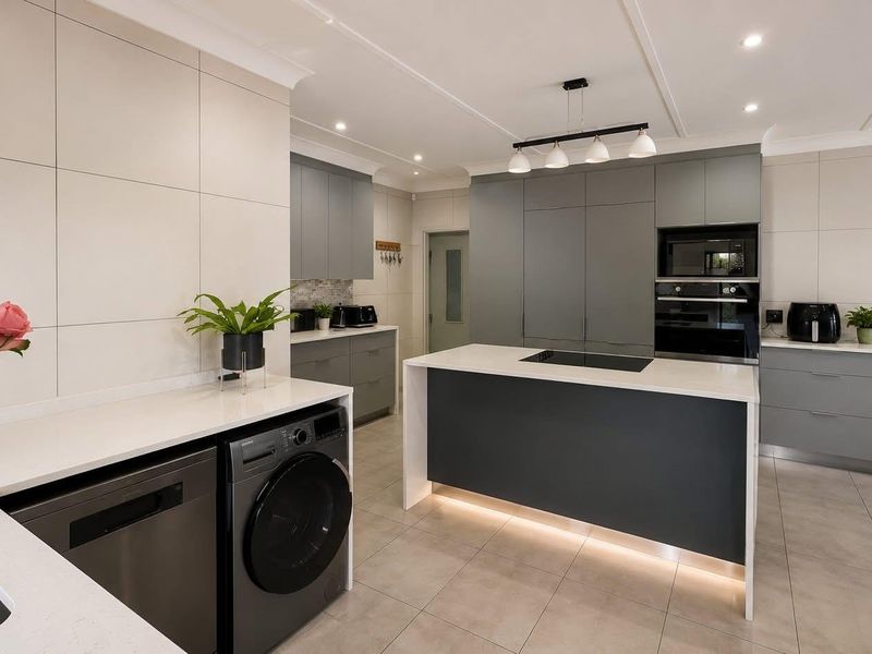 Modern, high-end kitchen featuring sleek grey cabinetry, a central island with integrated cooktop, stone countertops, and premium built-in appliances.