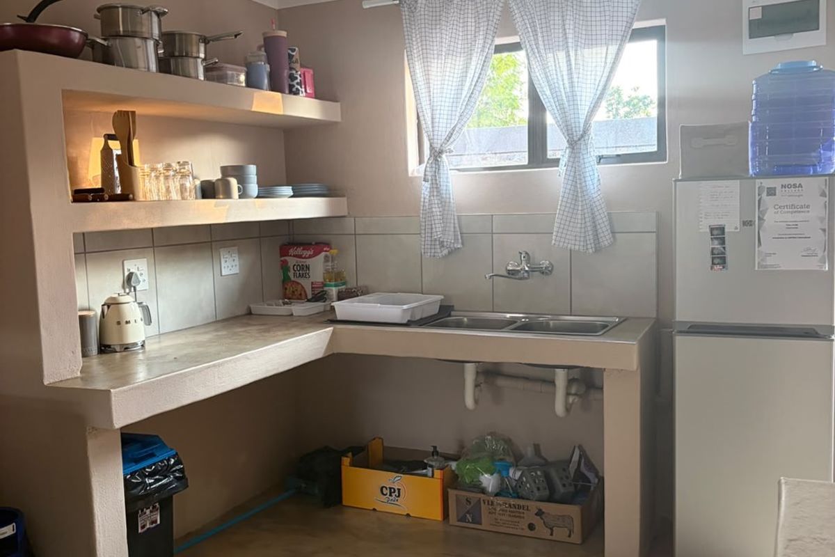 A functional kitchen area featuring built-in concrete shelving, a double basin sink, and tiled splashback, offering a basic layout with potential for modernization.