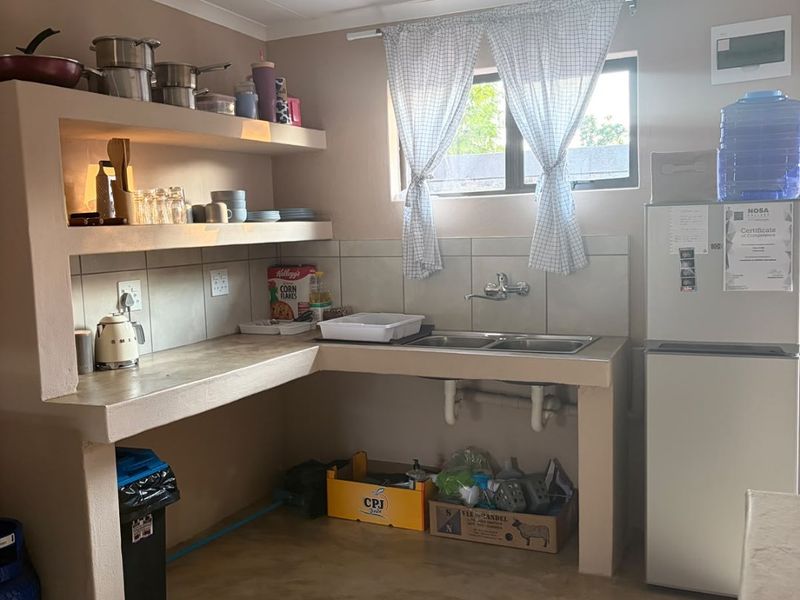 A functional kitchen area featuring built-in concrete shelving, a double basin sink, and tiled splashback, offering a basic layout with potential for modernization.