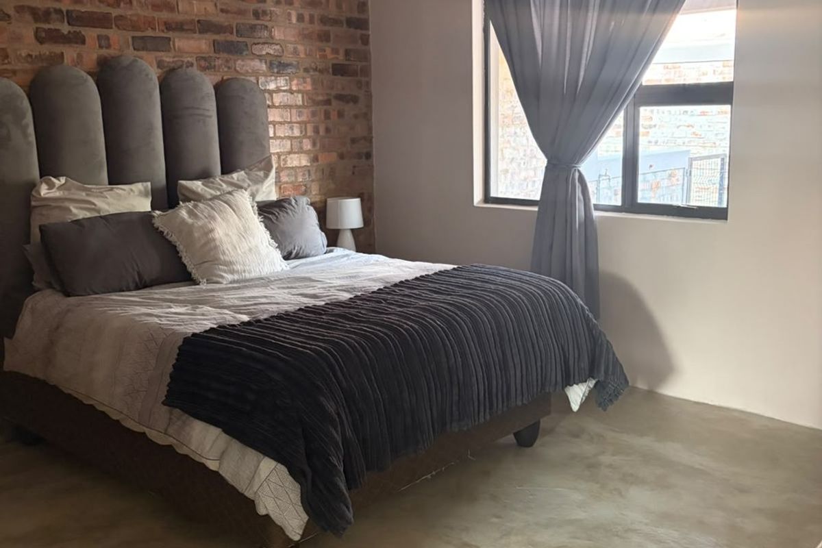 A well-lit bedroom featuring a rustic exposed brick feature wall and modern polished concrete flooring, creating a contemporary industrial aesthetic.