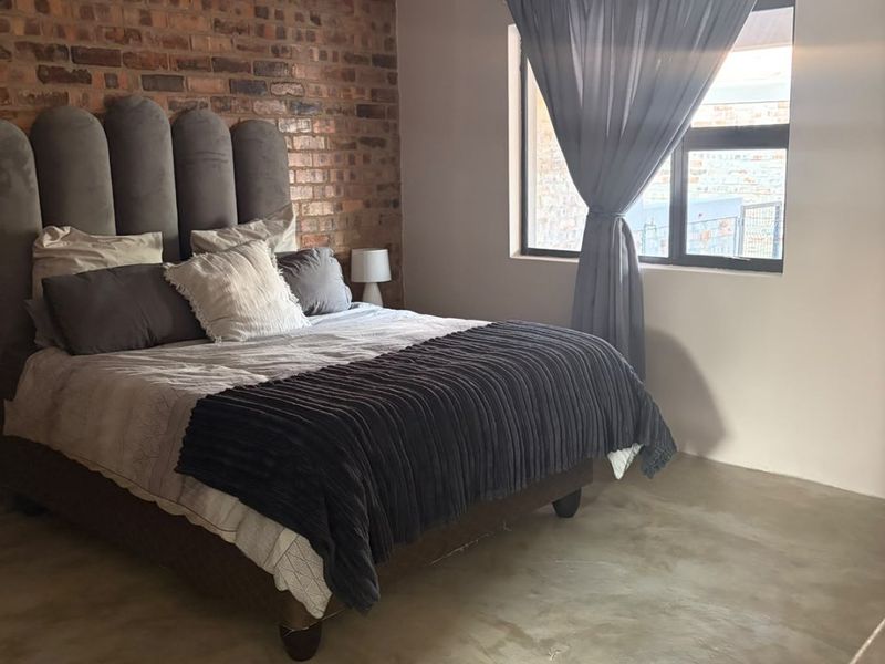 A well-lit bedroom featuring a rustic exposed brick feature wall and modern polished concrete flooring, creating a contemporary industrial aesthetic.