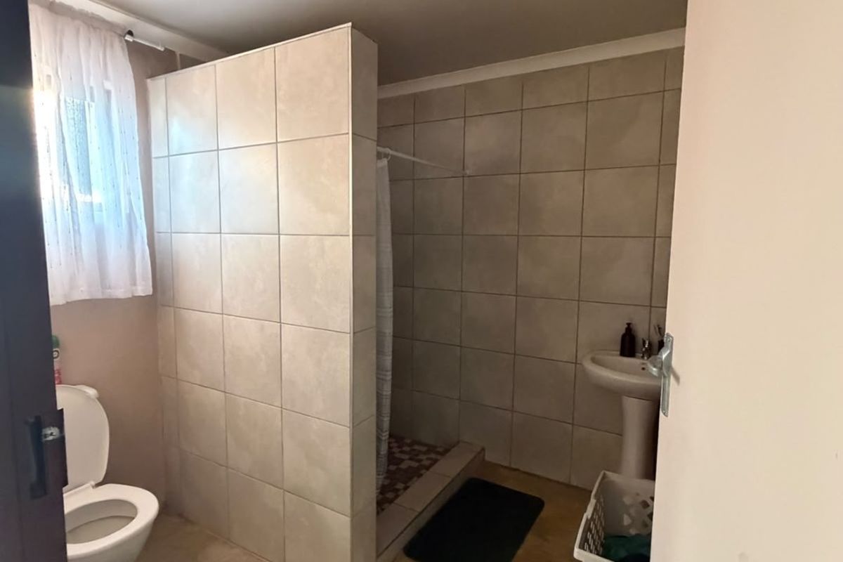A functional bathroom featuring a tiled shower enclosure, pedestal basin, and toilet with neutral wall tiling.