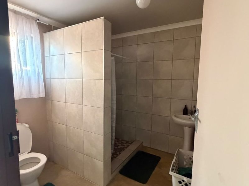 A functional bathroom featuring a tiled shower enclosure, pedestal basin, and toilet with neutral wall tiling.