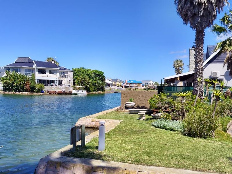 A scenic view of the canal waterfront featuring a landscaped garden, stone retaining wall, and surrounding residential properties.