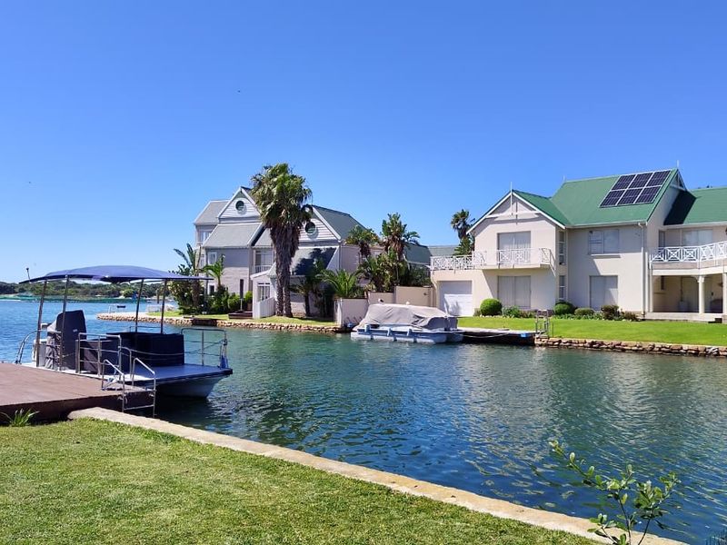 A scenic view of waterfront residential properties featuring private canal access, manicured lawns, and well-maintained architectural exteriors with solar installations.