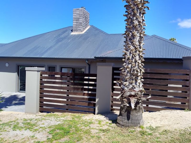 Rear view of the property featuring a corrugated metal roof, stone chimney, and a private paved patio area enclosed by timber slat fencing.