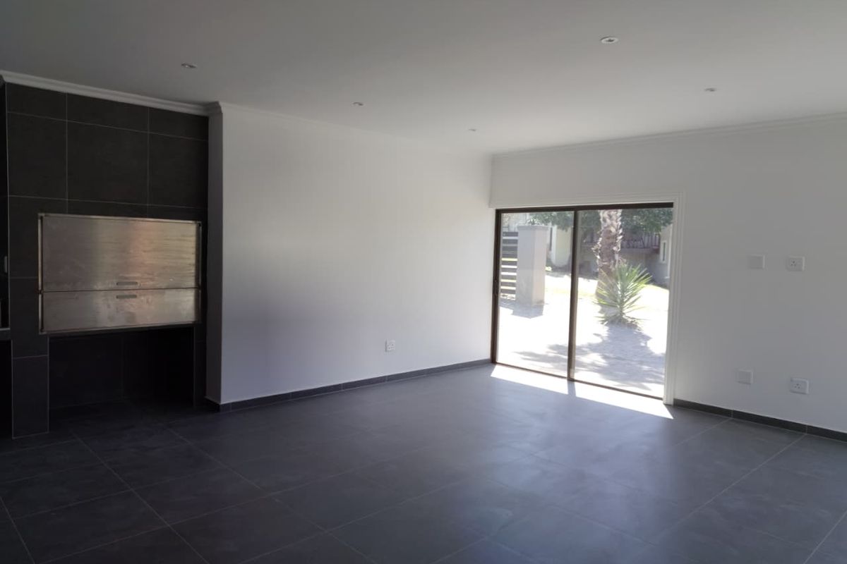 Spacious living area featuring modern dark floor tiles, recessed lighting, and a built-in braai, with direct access to the garden through a sliding door.