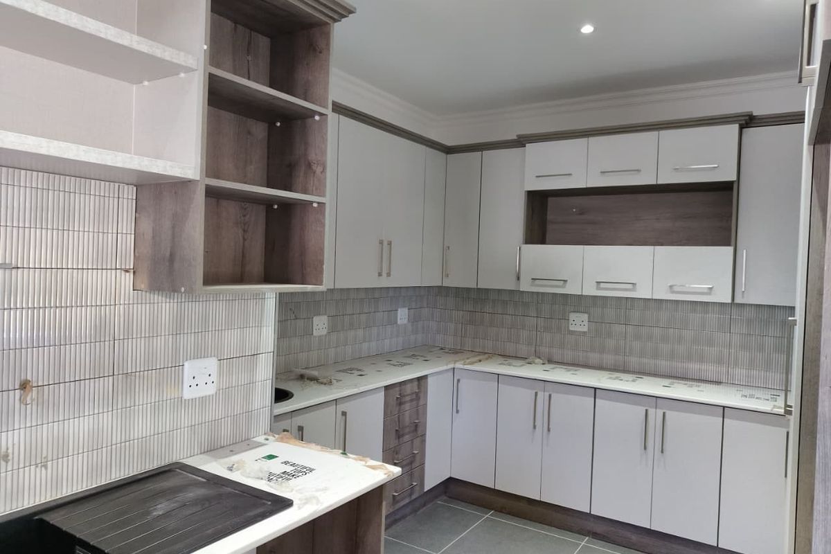 Modern kitchen featuring clean white and wood-tone cabinetry, tiled backsplash, and durable tiled flooring, offering a fresh and functional workspace.