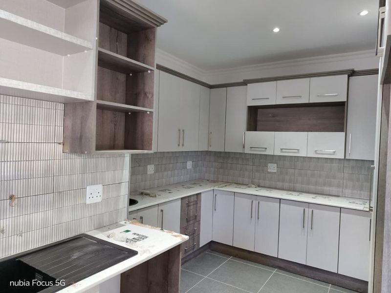 Modern kitchen featuring clean white and wood-tone cabinetry, tiled backsplash, and durable tiled flooring, offering a fresh and functional workspace.