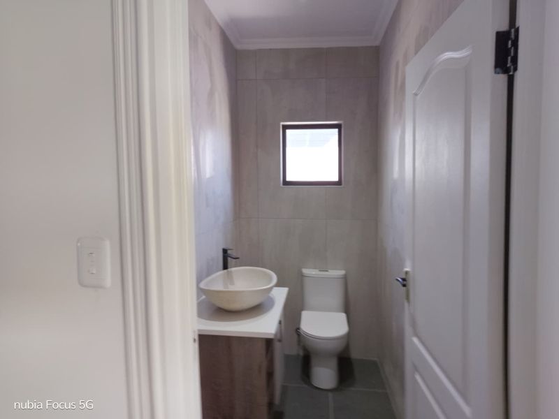 A compact, modern bathroom featuring a vessel sink on a vanity cabinet, a toilet, and neutral wall and floor tiling.