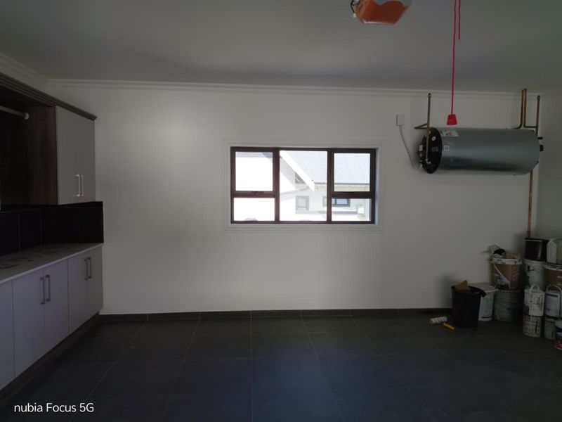 A spacious garage featuring tiled flooring, built-in storage cabinetry, a window, and a wall-mounted electric geyser.