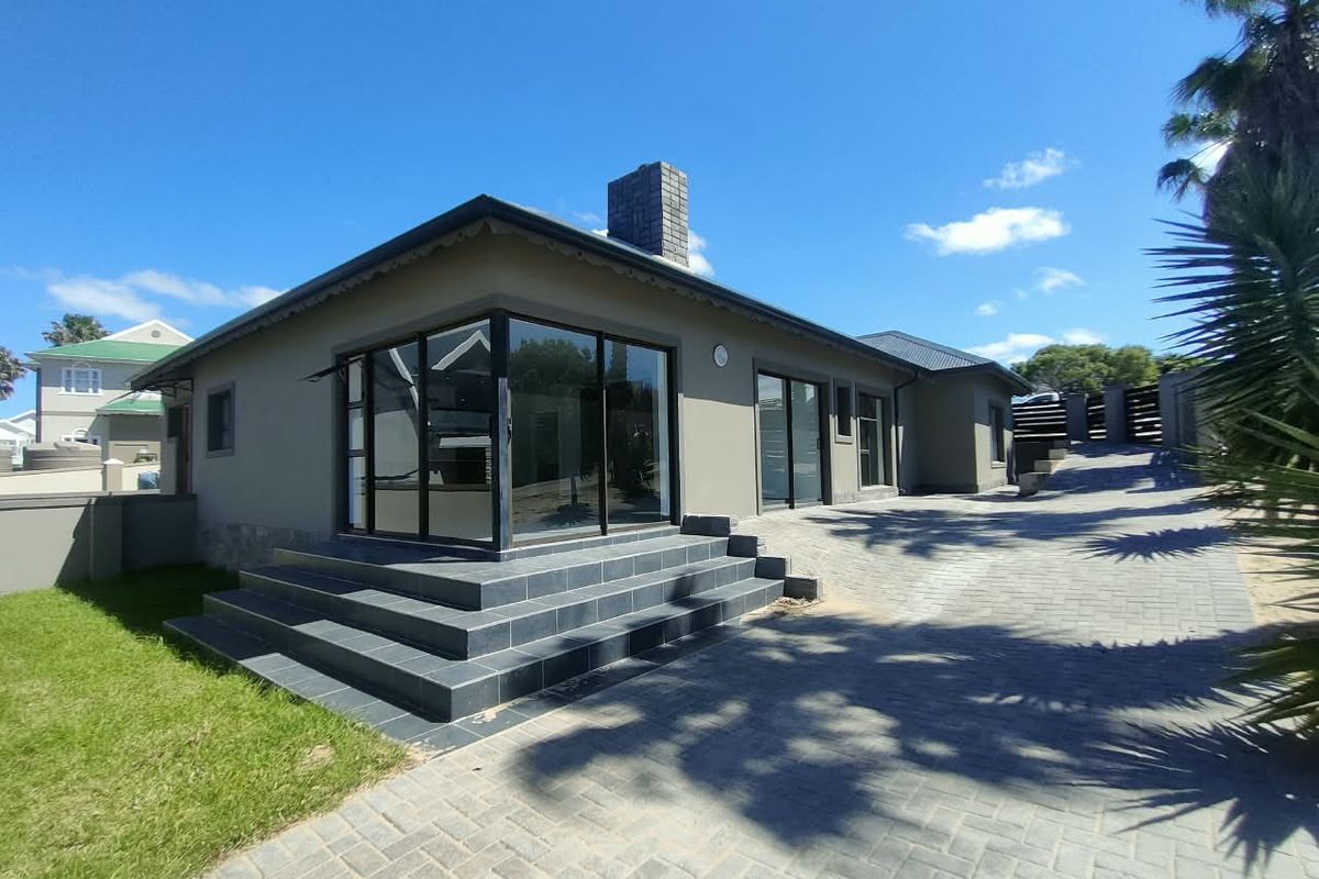Rear exterior view of the house featuring a paved driveway, tiled patio steps, and large sliding glass doors leading into the living area.