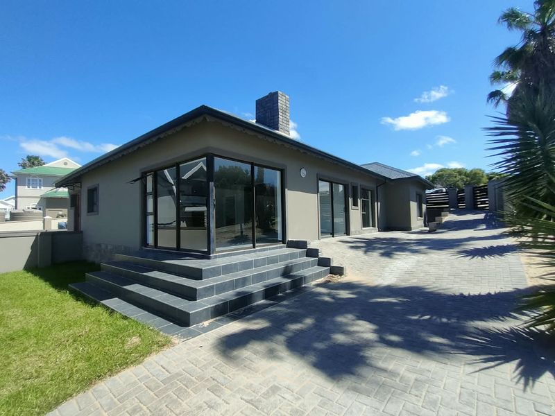 Rear exterior view of the house featuring a paved driveway, tiled patio steps, and large sliding glass doors leading into the living area.