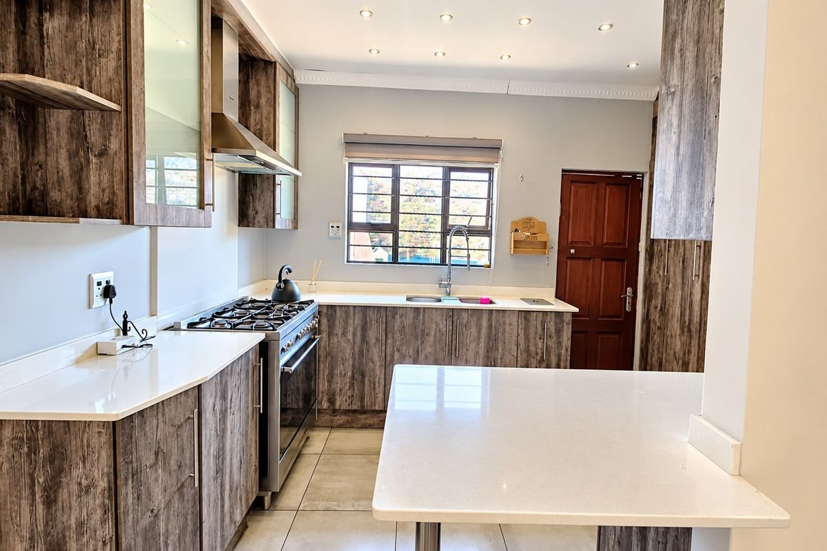 Modern kitchen featuring wood-grain cabinetry, quartz countertops, a gas stove with extractor fan, and recessed lighting, offering a clean and functional workspace.