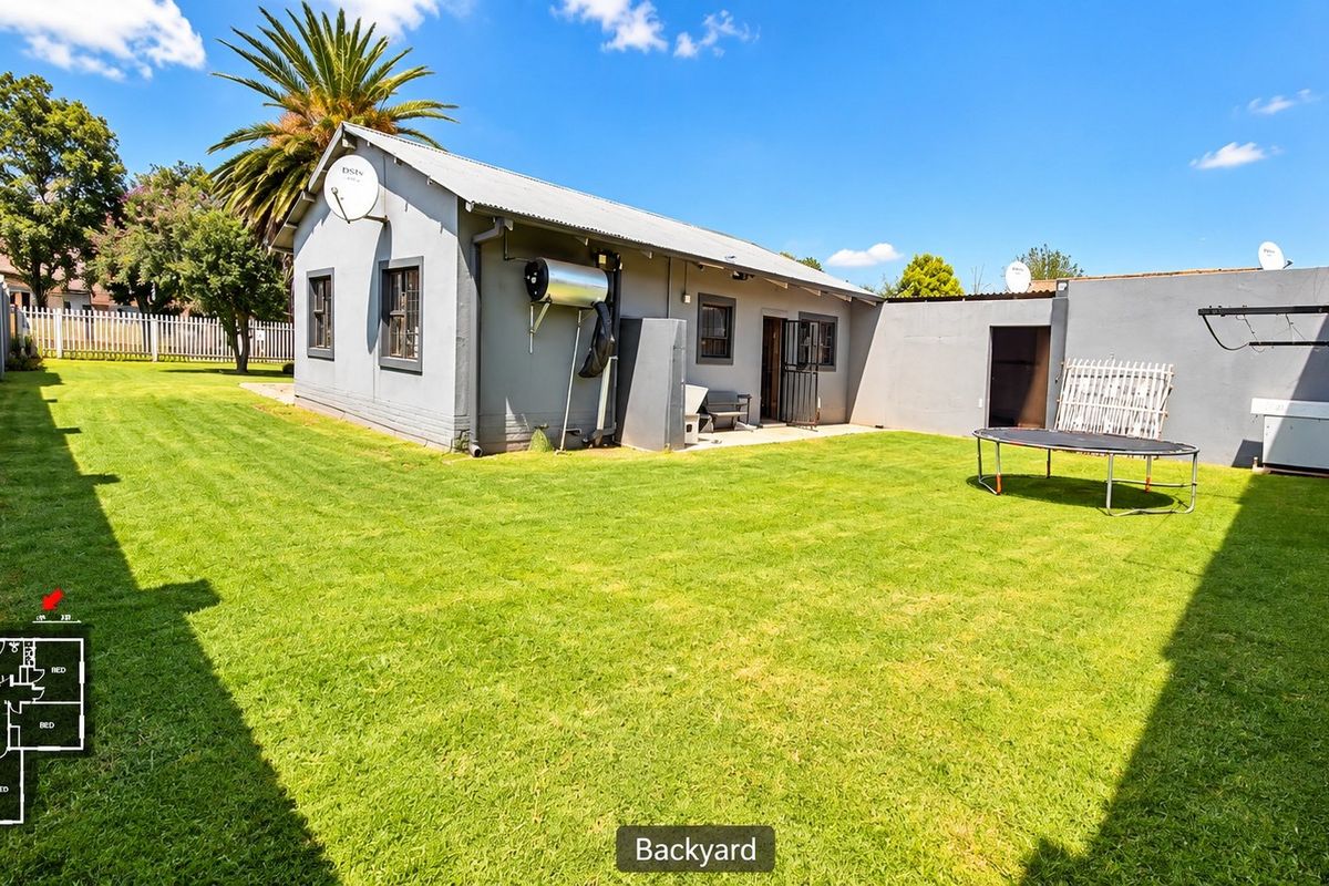 Rear view of the property featuring a spacious lawn, solar geyser, and secure boundary walling.
