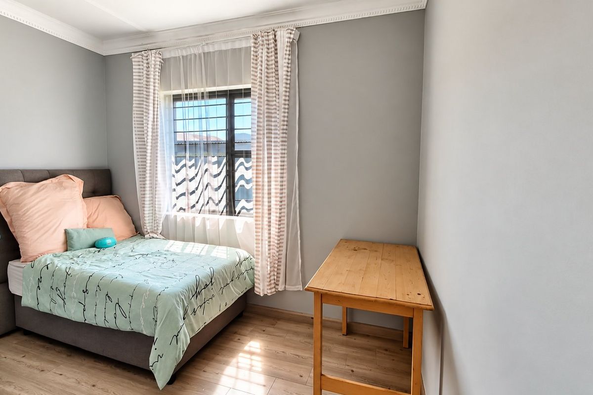 A well-maintained bedroom featuring laminate flooring, crown molding, and a window fitted with security bars.