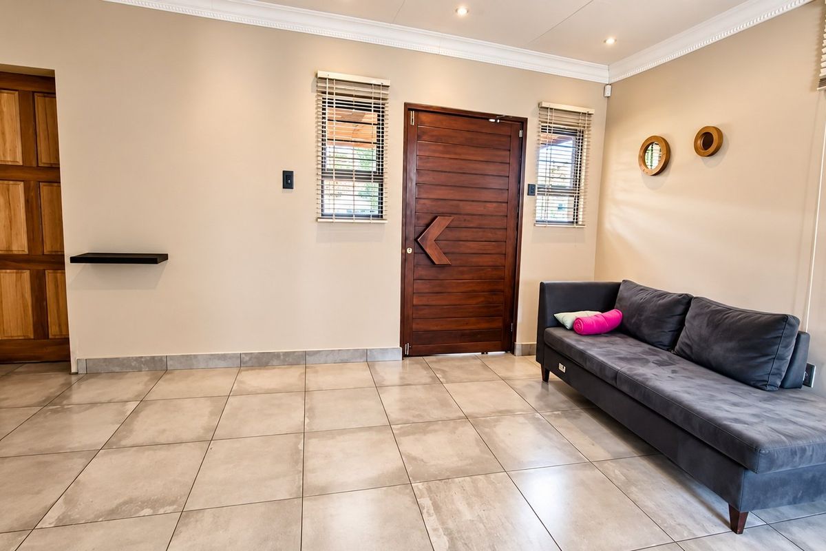 A bright and well-maintained living area featuring large format floor tiles, a solid wooden entrance door, and modern recessed lighting.