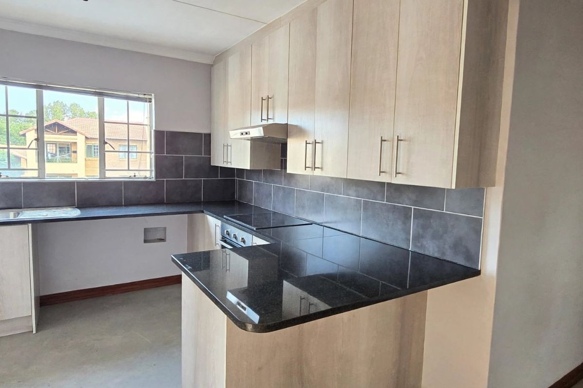 A functional kitchen featuring light wood-finish cabinetry, dark granite countertops, a tiled backsplash, and integrated cooking appliances.