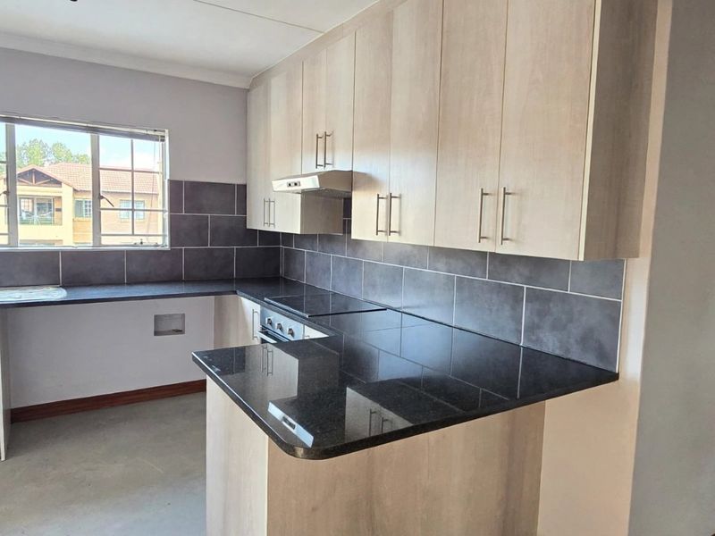 A functional kitchen featuring light wood-finish cabinetry, dark granite countertops, a tiled backsplash, and integrated cooking appliances.