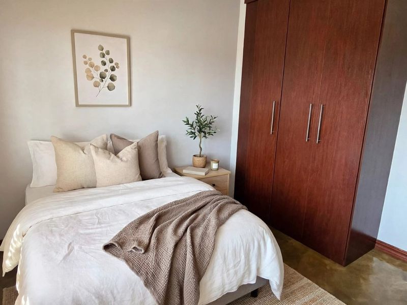 A well-maintained bedroom featuring a large built-in wardrobe, polished concrete flooring, and venetian blinds, offering a clean and functional living space.