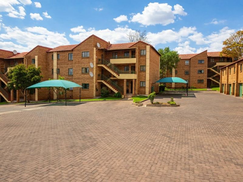 Exterior view of a multi-story apartment complex featuring face brick construction, tiled roofs, paved parking areas, and covered carports.