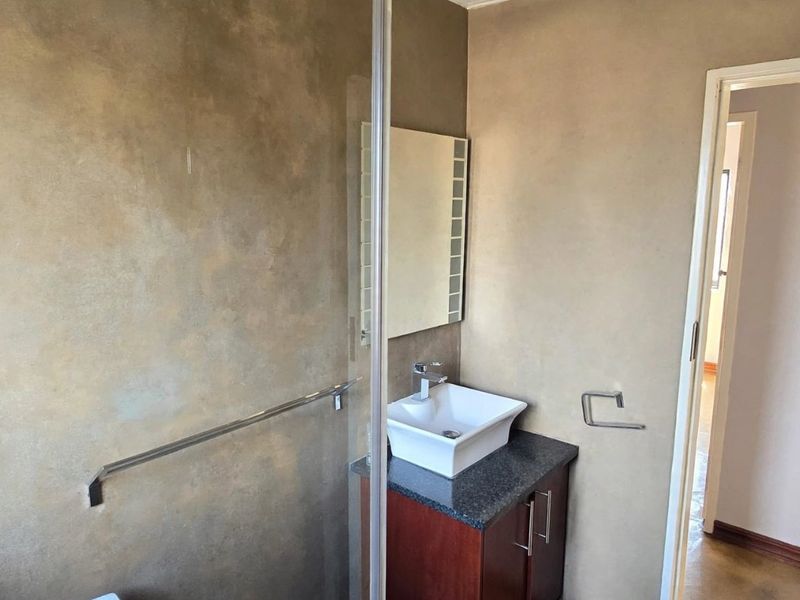A modern bathroom featuring a vessel sink on a granite vanity, a glass shower screen, and neutral textured wall finishes.