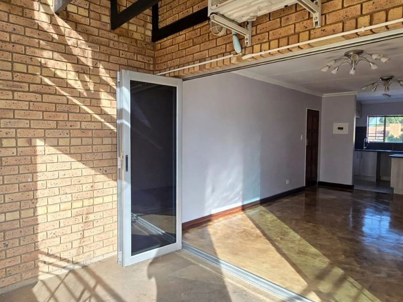 An open-plan living and kitchen area featuring polished concrete floors, exposed brickwork, and seamless access to an outdoor patio through large sliding glass doors.