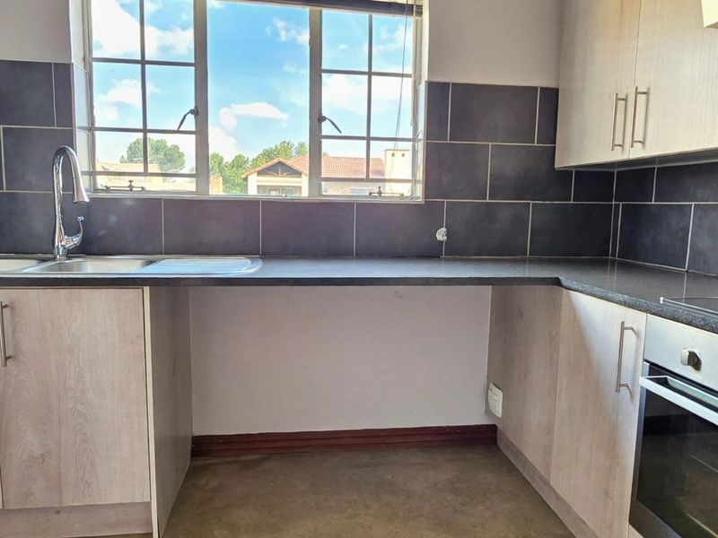 A functional kitchen featuring built-in cabinetry, a stainless steel sink, and integrated oven and hob, with dark tiled backsplash and ample counter space.