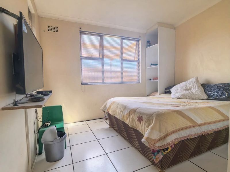 A functional bedroom featuring tiled flooring, built-in shelving, and a window with blinds, offering a basic layout ready for cosmetic updates.