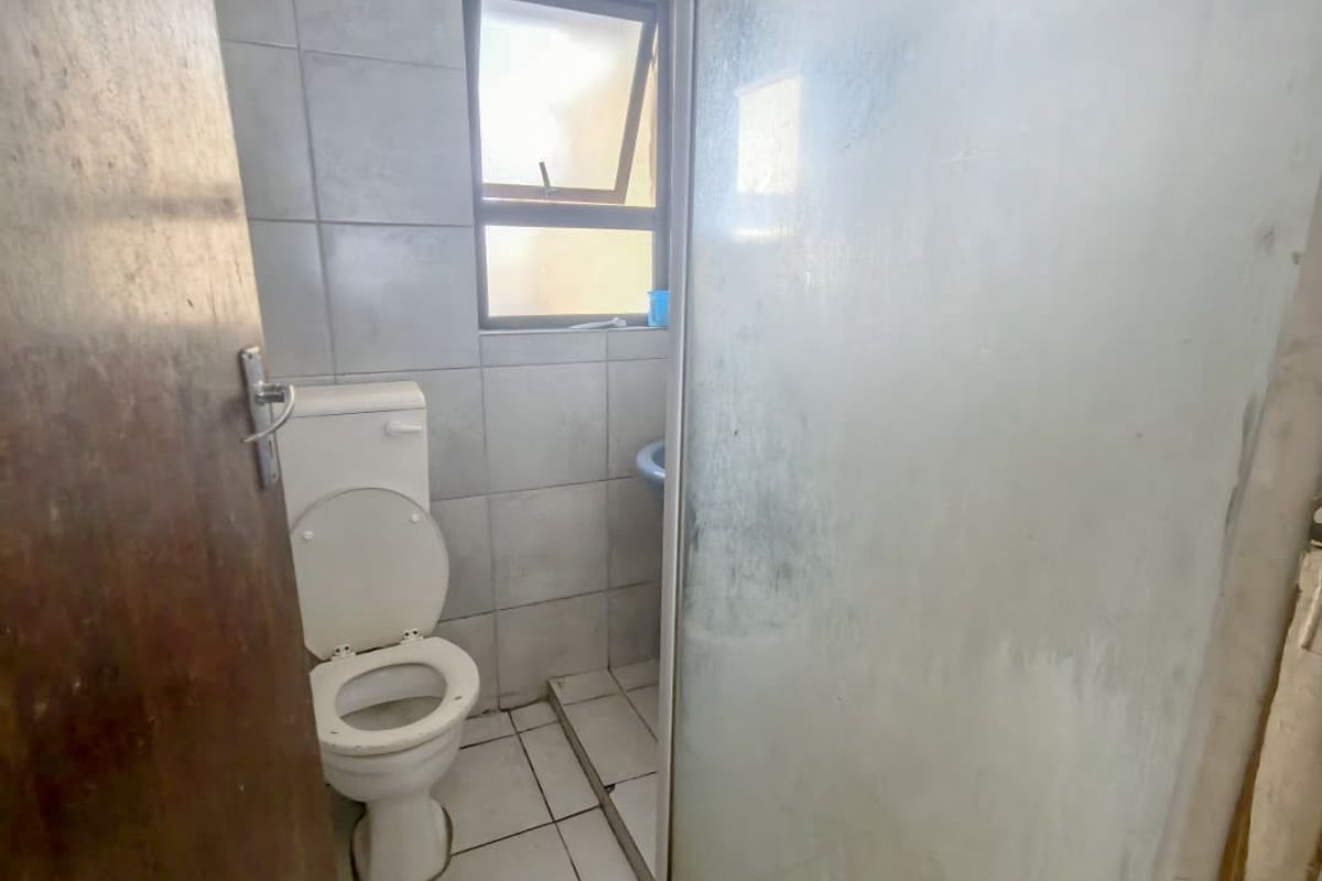 A compact bathroom featuring a toilet, tiled finishes, and a shower enclosure, requiring some maintenance and cosmetic updates.
