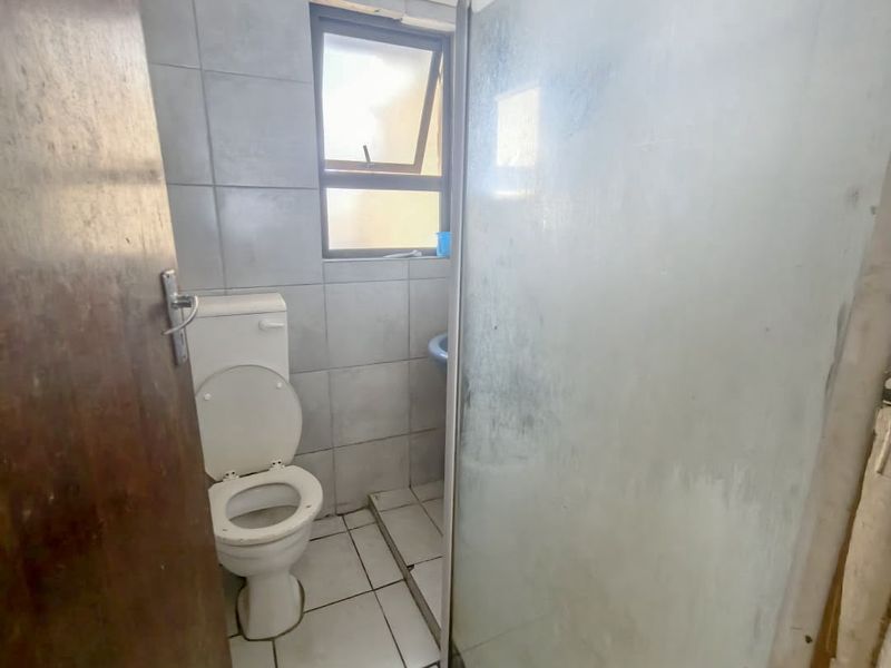 A compact bathroom featuring a toilet, tiled finishes, and a shower enclosure, requiring some maintenance and cosmetic updates.