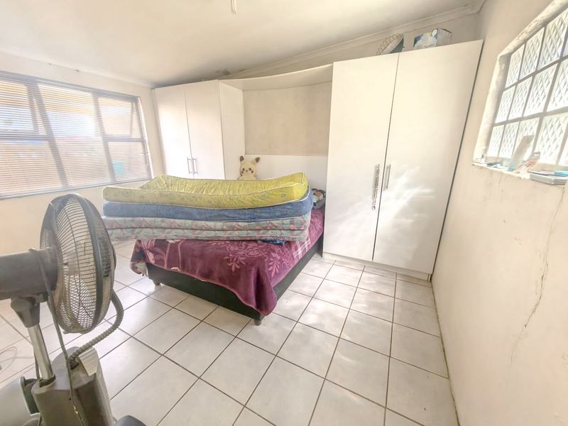 A bedroom featuring built-in cupboards, tiled flooring, and aluminium window frames. The room requires cosmetic updates to address wall cracks and surface wear.