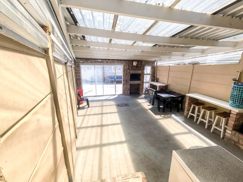 Covered outdoor patio area featuring a built-in braai, concrete flooring, and translucent roof sheeting, providing a functional space for outdoor entertaining.