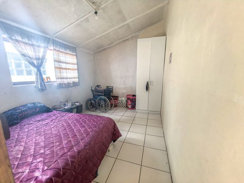 A bedroom featuring tiled flooring, a built-in wardrobe, and a sloped ceiling, requiring cosmetic updates to the walls and ceiling finishes.