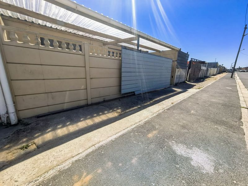 Street view showing the property boundary wall, sliding gate, and covered parking structure along the sidewalk.