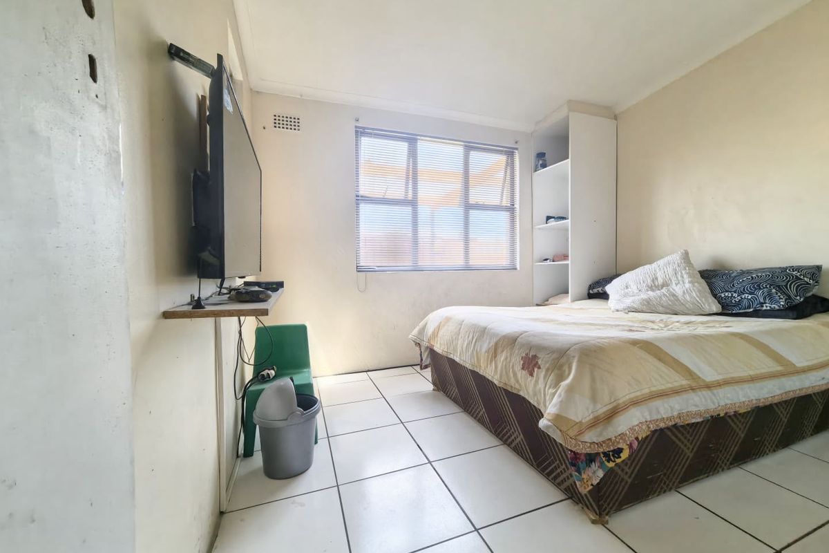 A functional bedroom featuring tiled flooring, built-in shelving, and a window with blinds, offering a basic layout ready for cosmetic updates.