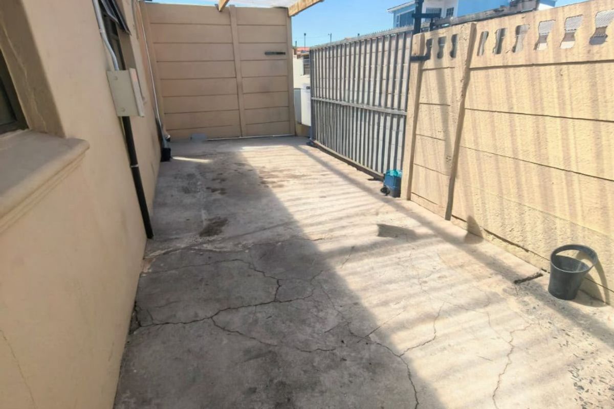 A covered outdoor patio area featuring a corrugated roof, concrete flooring, and secure boundary walls, suitable for a utility or storage space.