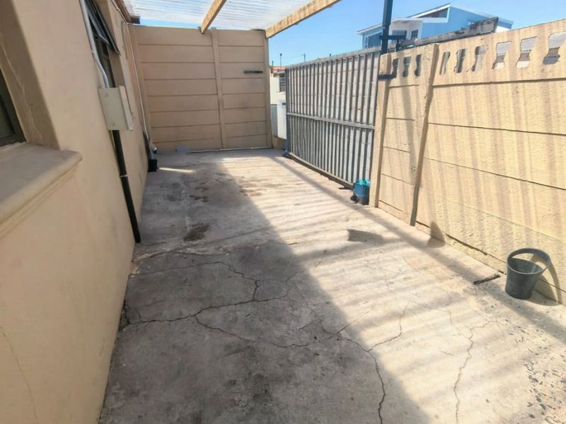 A covered outdoor patio area featuring a corrugated roof, concrete flooring, and secure boundary walls, suitable for a utility or storage space.