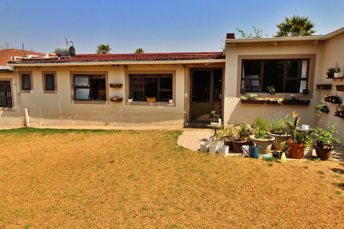 Rear view of the property featuring a paved patio area, aluminium window frames, and a solar water heater installed on the tiled roof.