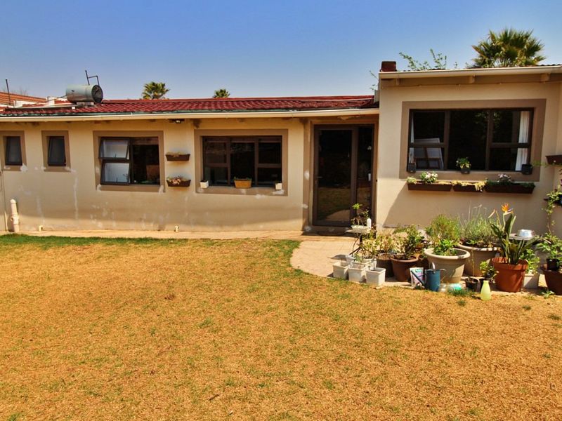 Rear view of the property featuring a paved patio area, aluminium window frames, and a solar water heater installed on the tiled roof.