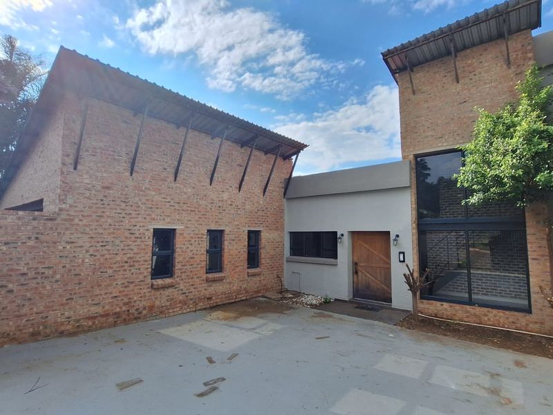 Front exterior view of a modern house featuring exposed brickwork, large glass windows, and a timber entrance door with a concrete driveway.