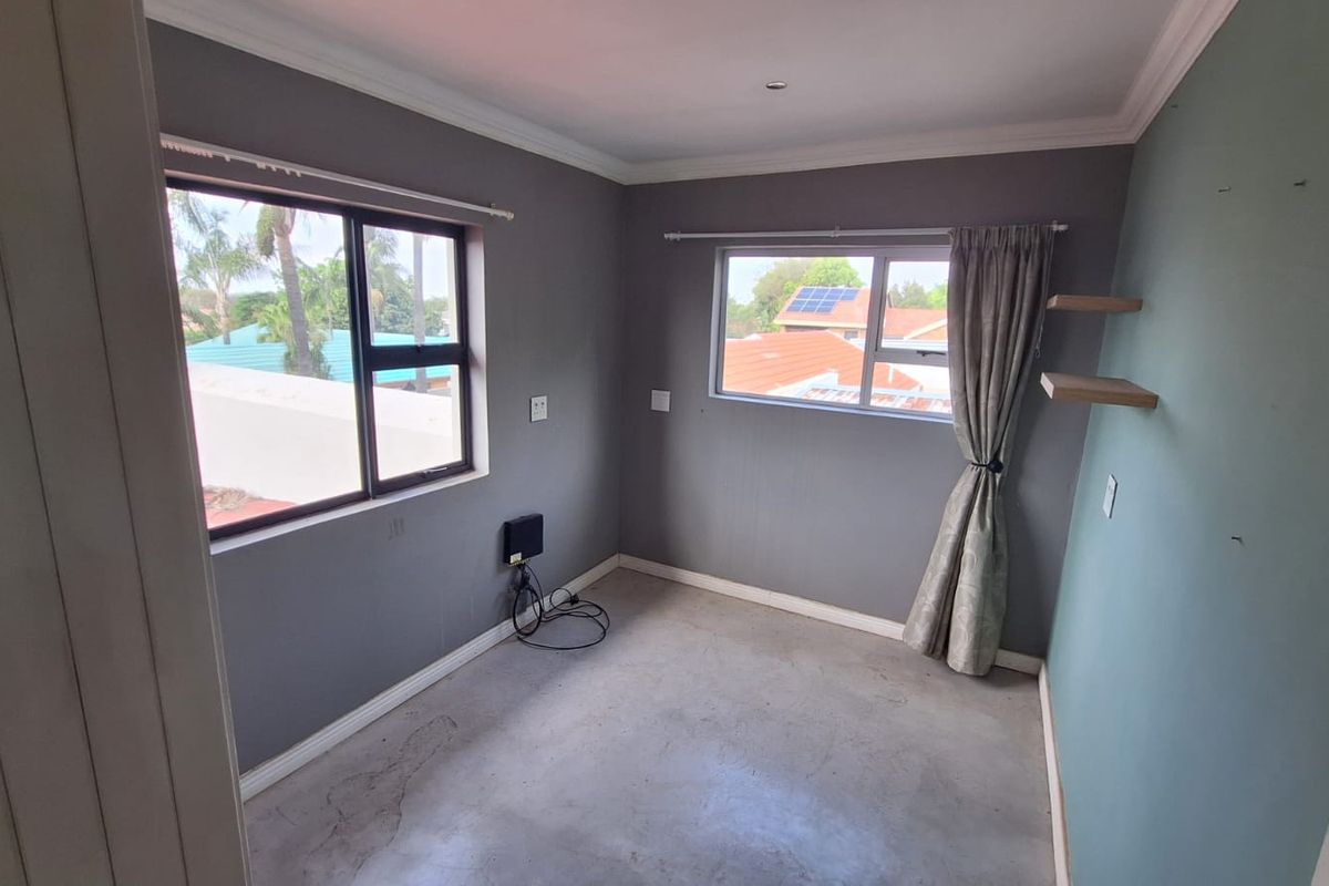 A vacant bedroom featuring grey walls, aluminium window frames, and exposed concrete flooring, offering a blank canvas for potential renovation or staging.