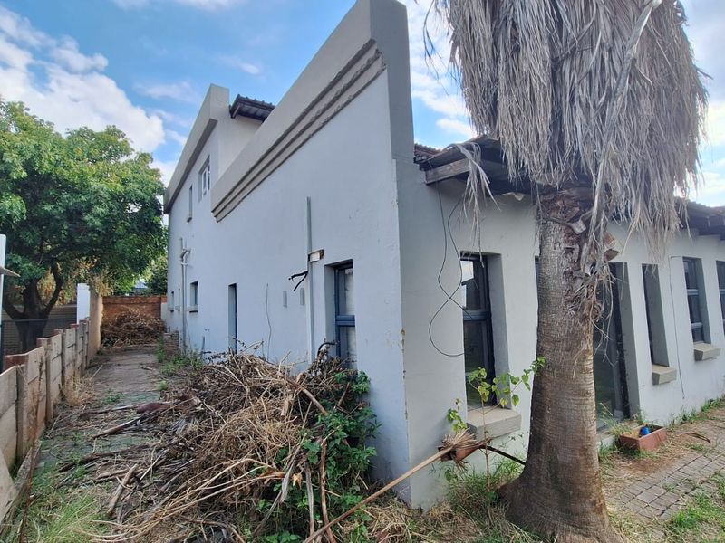 Rear exterior view of the property showing a paved walkway, brick boundary wall, and significant maintenance required for the garden and building facade.