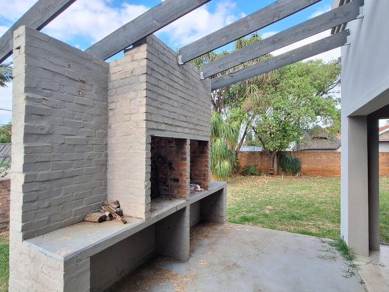 Outdoor patio area featuring a built-in brick braai, concrete prep surface, and timber pergola structure overlooking the garden.