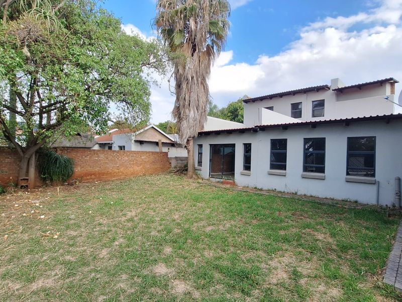 Rear view of the property featuring a private garden, brick boundary wall, paved walkway, and access to the home via a sliding glass door.